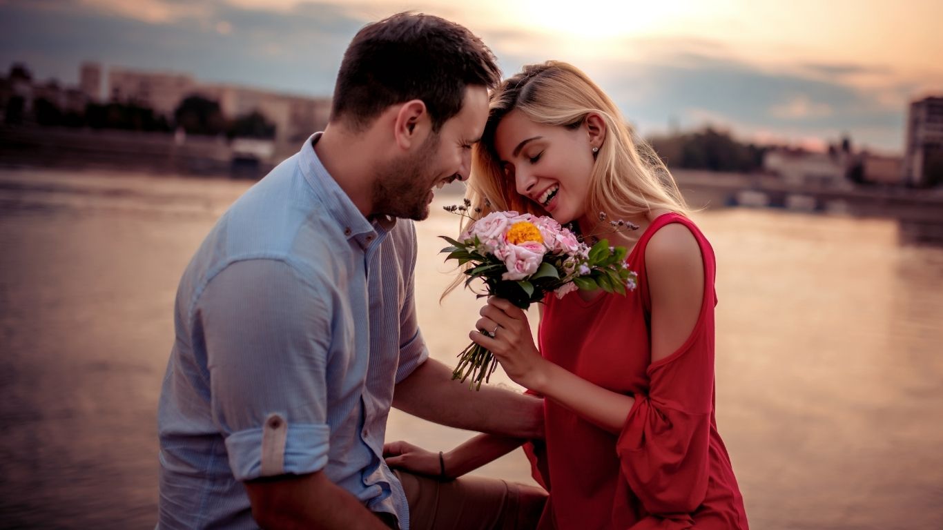 Hombre sorprende a su pareja con un ramo de flores al atardecer, mostrando el valor de los detalles en una relación."