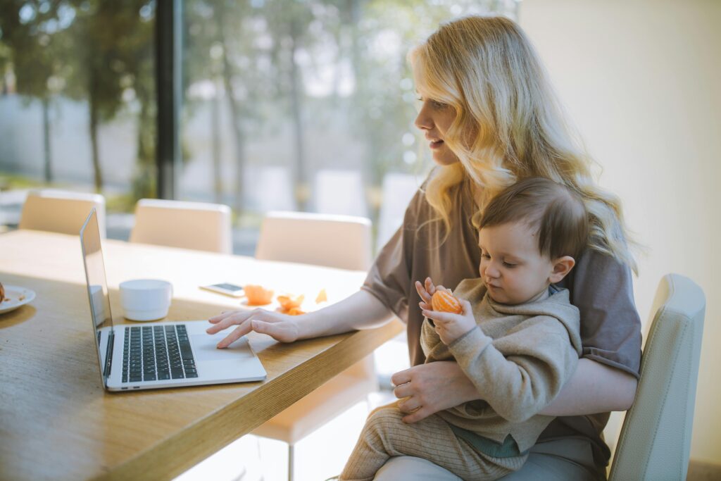 Madre trabajando en su computadora mientras cuida a su bebe.