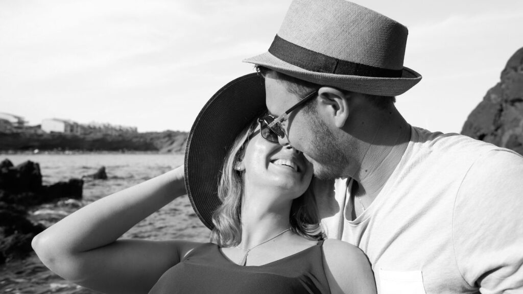 "Love captured in timeless moments. Smiling couple sharing a romantic moment by the seaside, wearing summer hats.