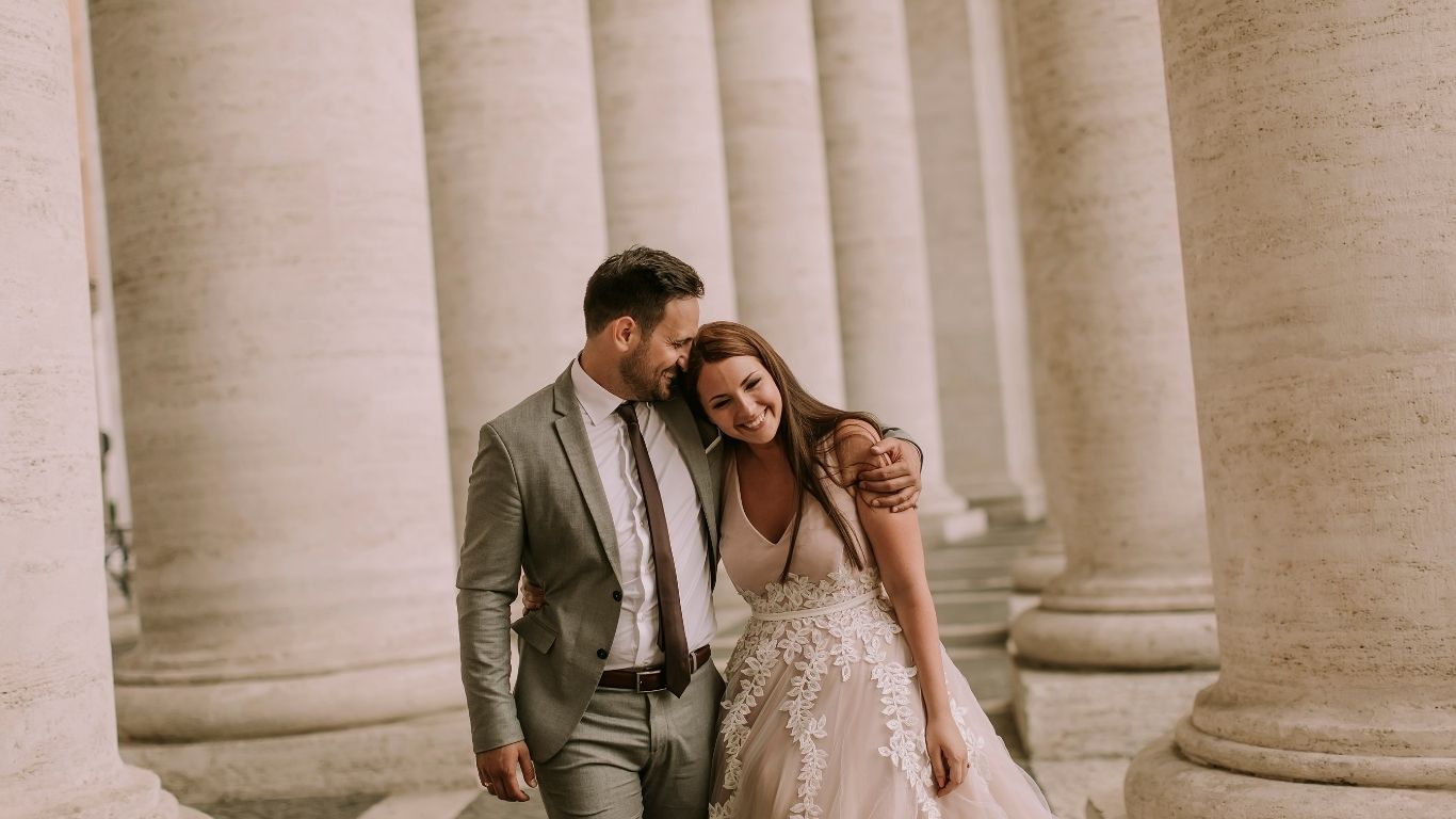 Happy couple walking arm in arm in elegant wedding attire, smiling with love